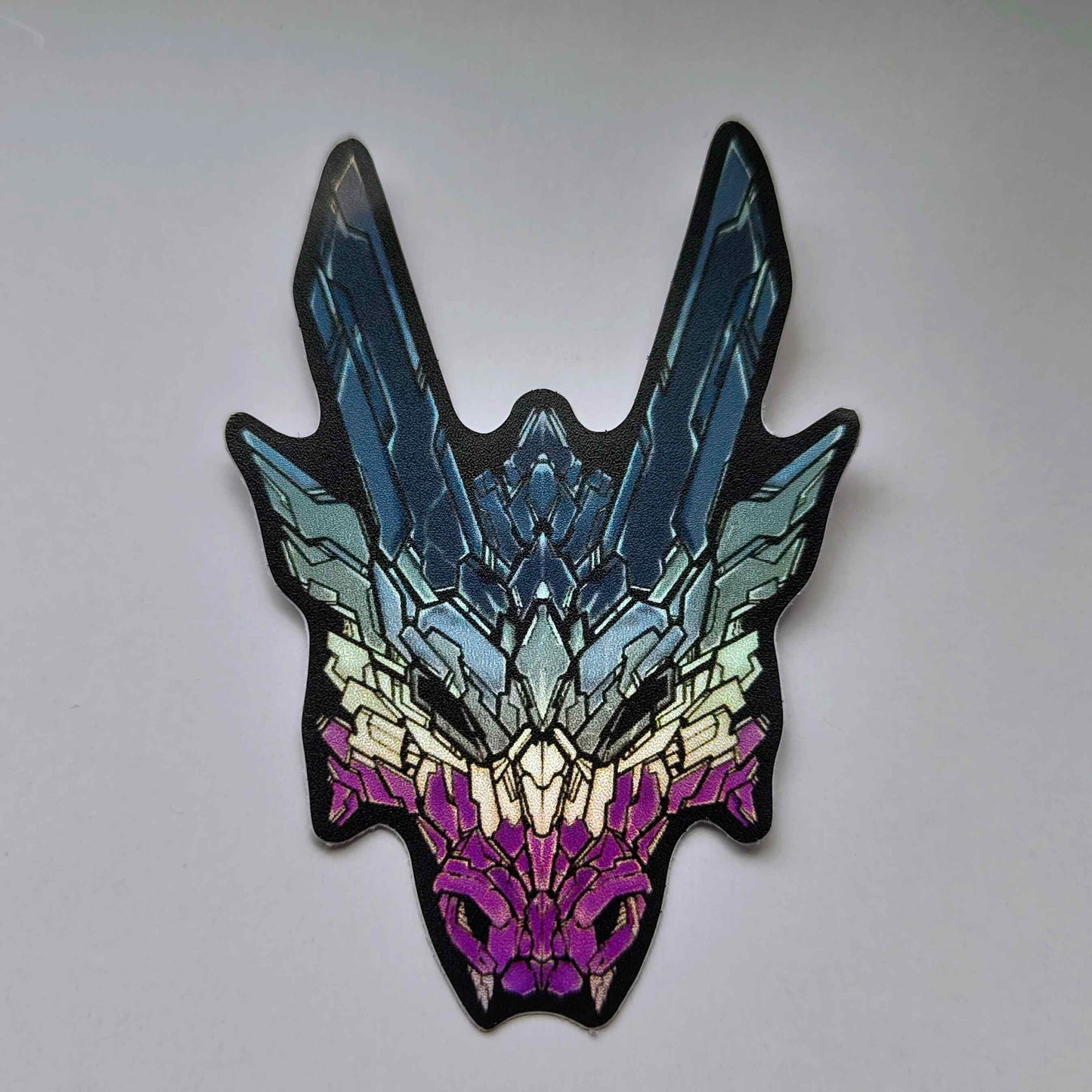 A special holographic sticker in XeneDragon's Generation Three DRGN design, the dragon head colors reflect the same colors as the ace pride flag
