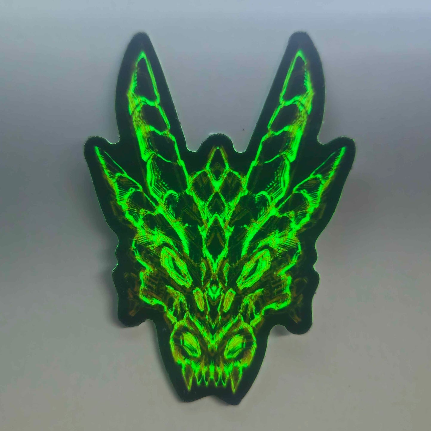 Shows the strong glow in the dark effect of the sticker that features an illustration of a dragon's skull in bright glowing green with orange circuit-like design in XeneDragon's art style.