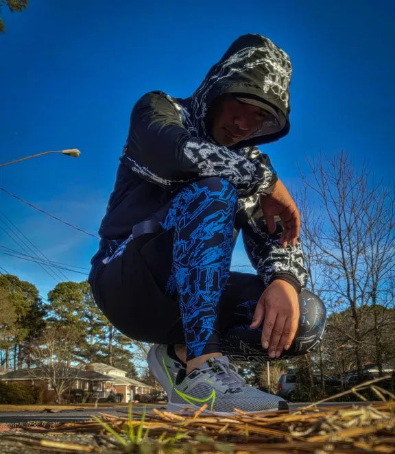A male model wearing the HYDRSNTH Leggings and shorts combo as well as the GLITCHDETH Crop jacket in a kneeling pose.