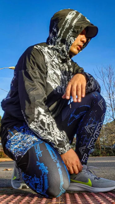 A male model wearing the HYDRSNTH Leggings and shorts combo as well as the GLITCHDETH Crop jacket in a kneeling pose.