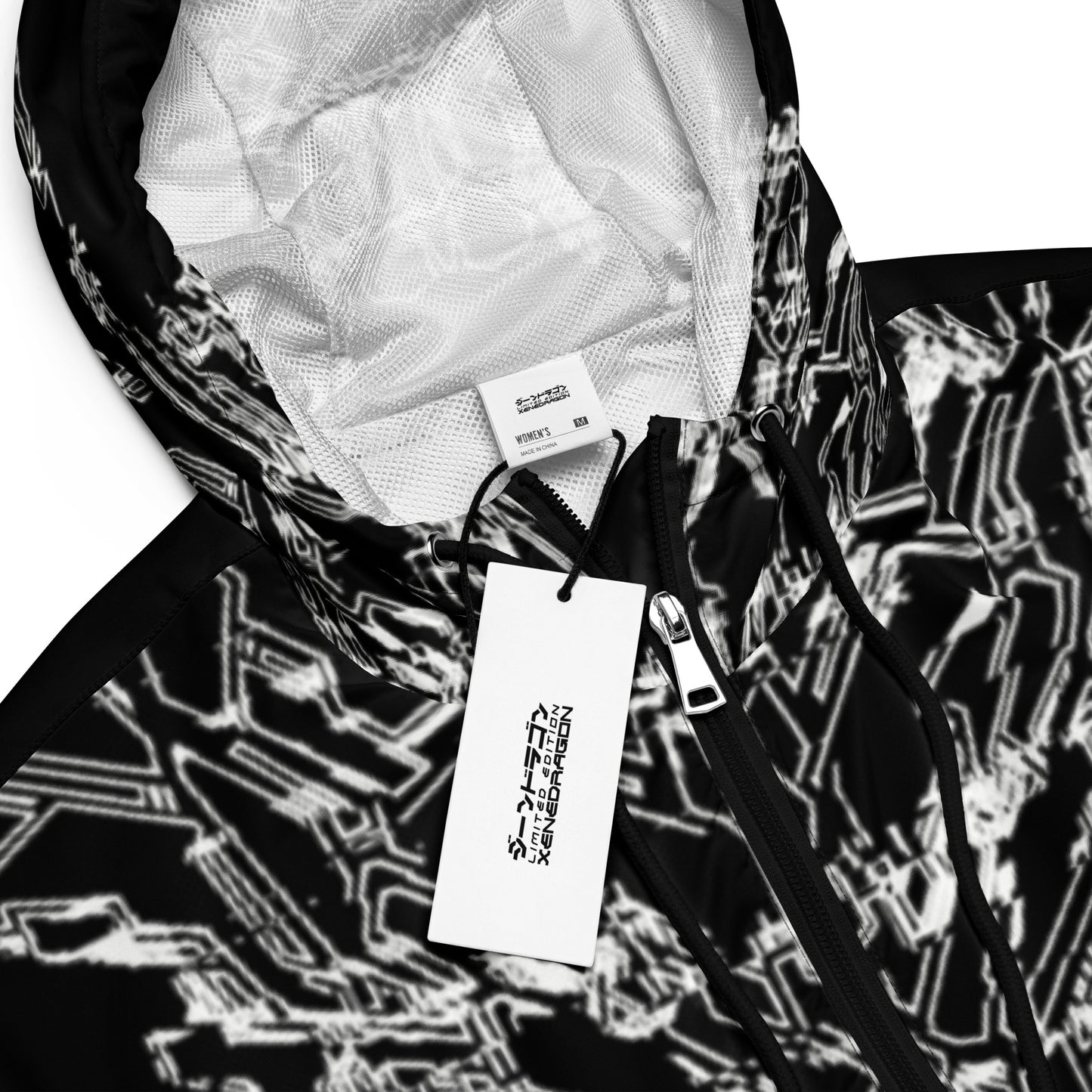 A close-up of a black cropped jacket with XeneDragon's white geometric pattern design. The cropped jacket has a zipper and a tag attached.
