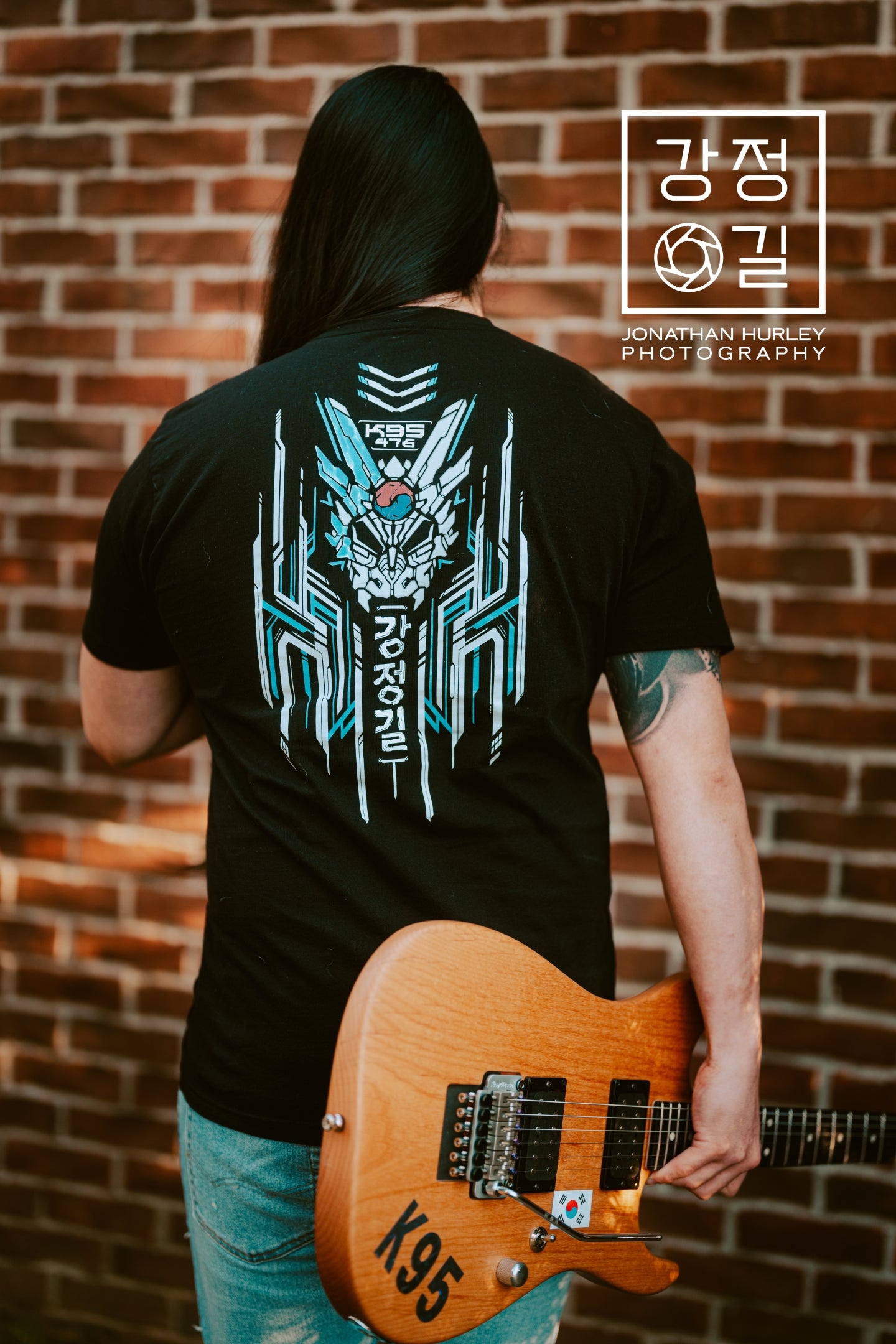 Talented guitarist Jonathan Hurley holding a guitar. He is modeling the black collaboration t-shirt showing the back design of the shirt.