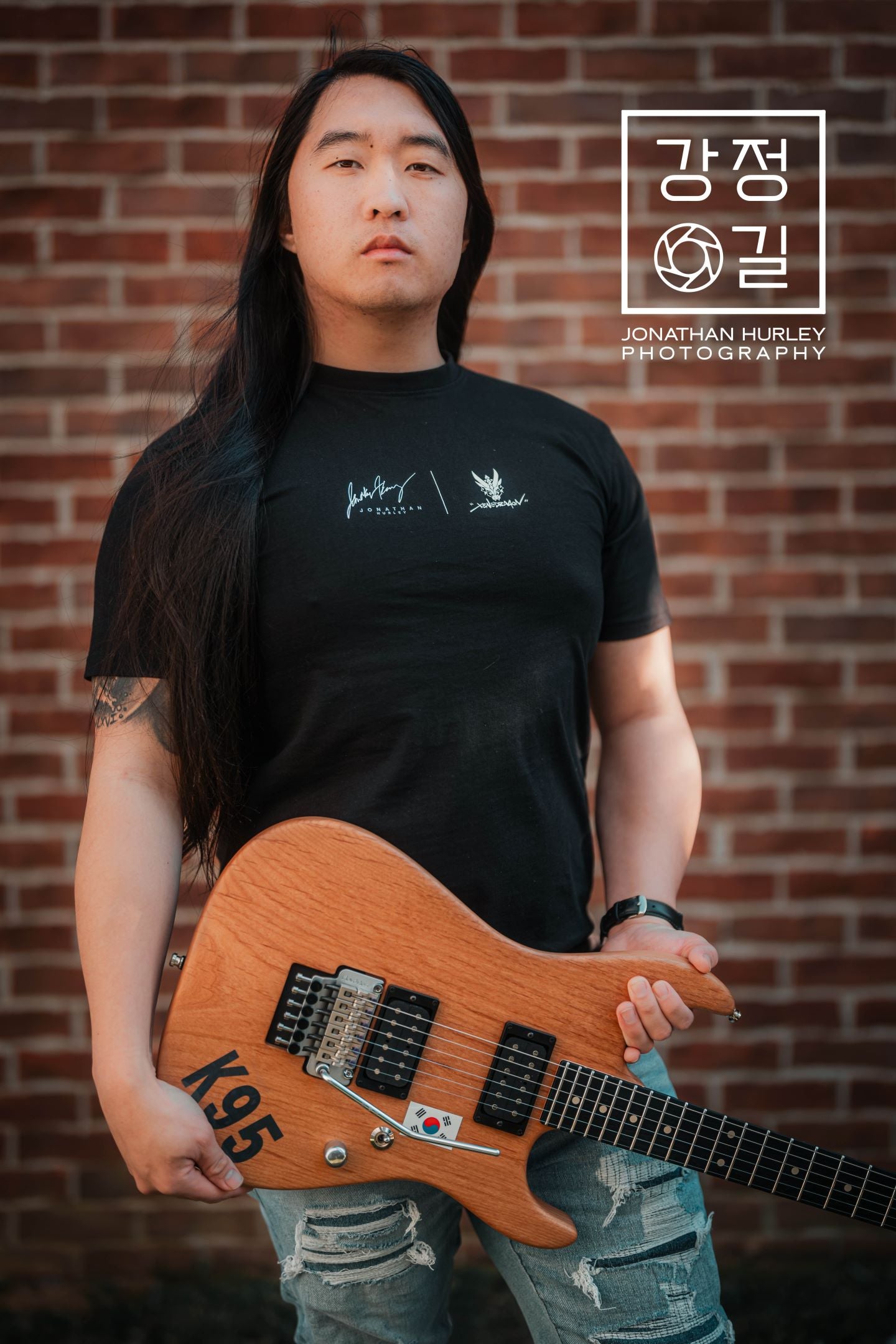 Talented guitarist Jonathan Hurley holding a guitar. He is modeling the black collaboration t-shirt showing the front design of the shirt.