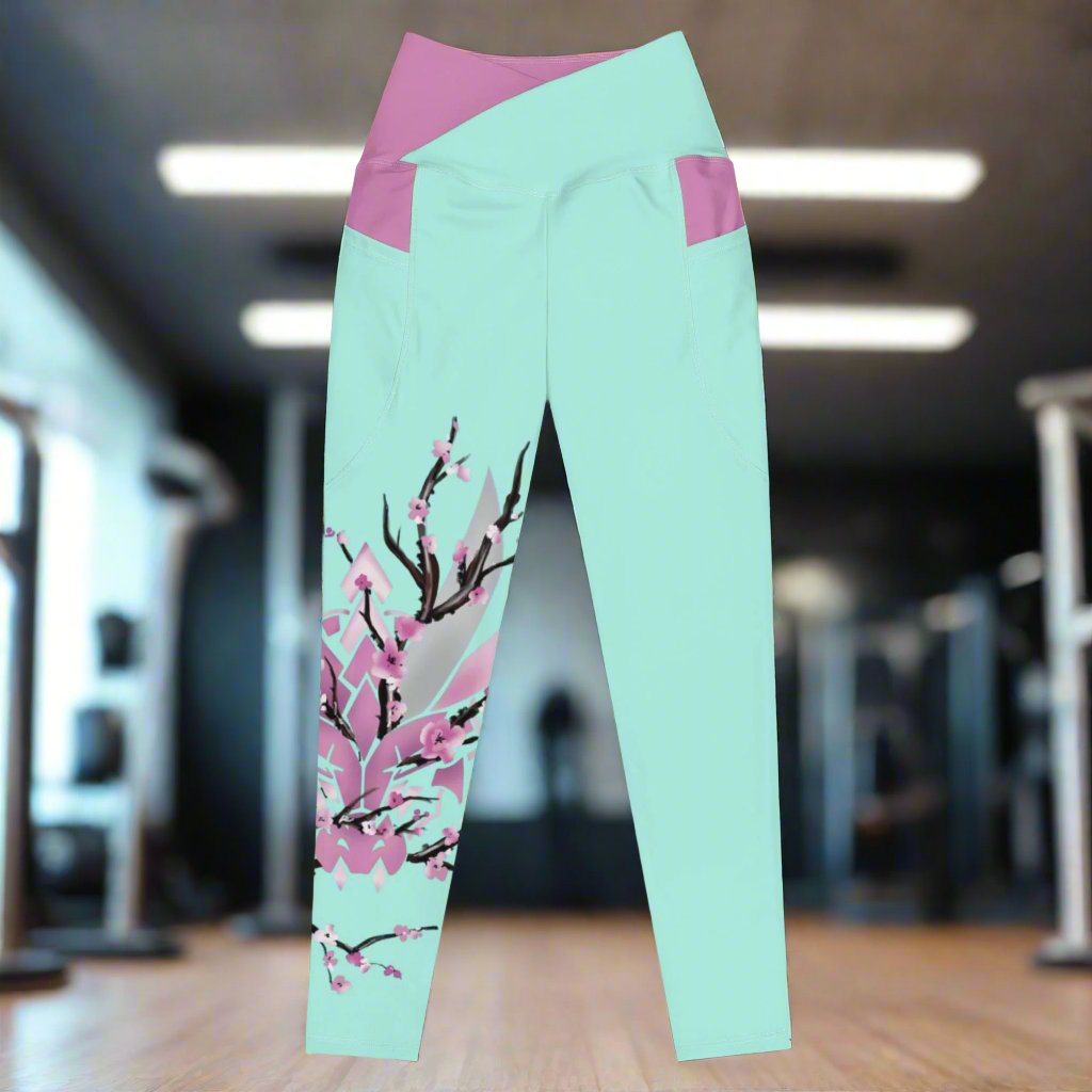A pair of light teal leggings with a pink waistband and pockets. Features a stylized dragon head with cherry blossoms surrounding it. Designed by XeneDragon.