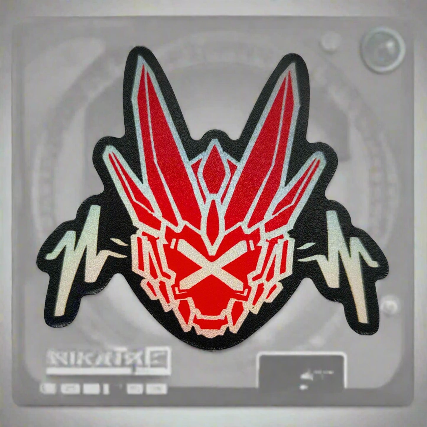 A sticker with a detailed design of a stylized dragon's head. The design features a dark background with a bright red, geometric shapes and two white, wavy lines below.