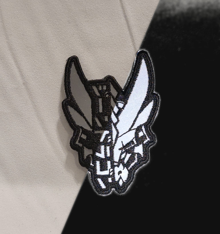 a black embroidery reflective mylar patch featuring XeneDragon's G1 Dragon design with katakana text variation. The left side of the picture shows that the patch looks like without reflection in room lighting. And the right side of the picture shows what the patch looks like when reflecting light at night.