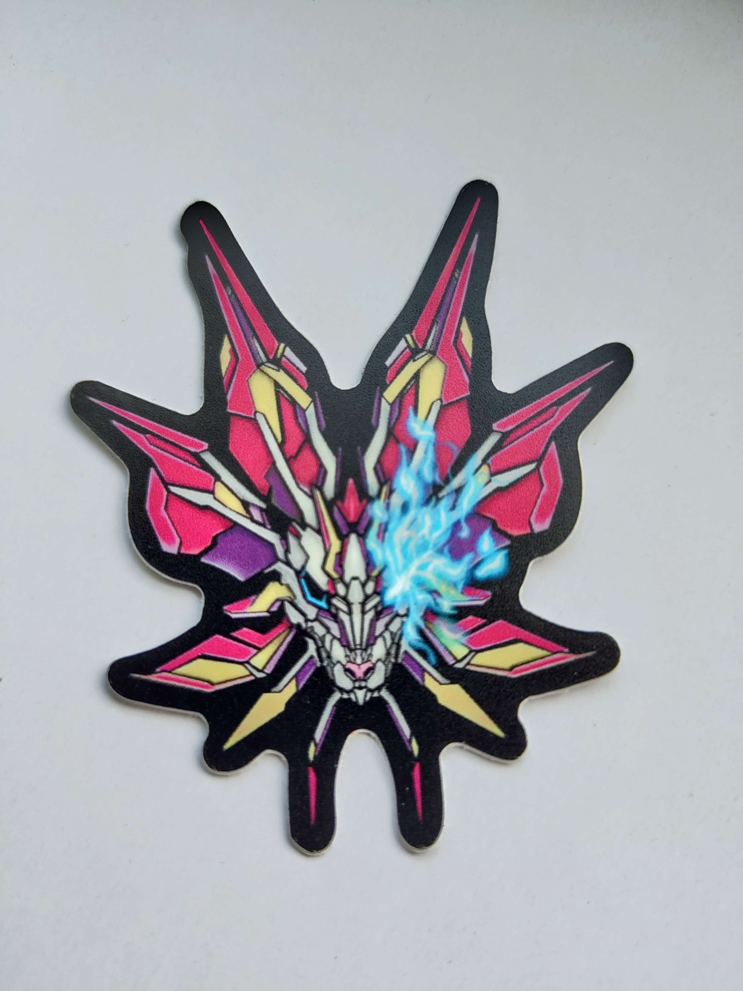 A sticker with a detailed design of a stylized monster's head. The design features vibrant colors like pink, yellow, and blue, with a prominent blue eye. Designed by XeneDragon