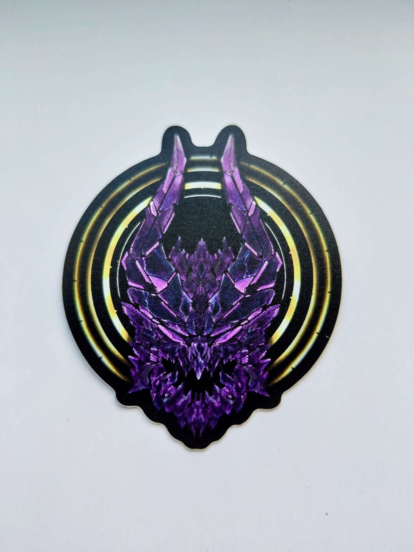 A sticker with a detailed design of a stylized dragon's head. The design features a dark color scheme with purple highlights and a gold circular designs behind the dragon's head. Designed by XeneDragon.