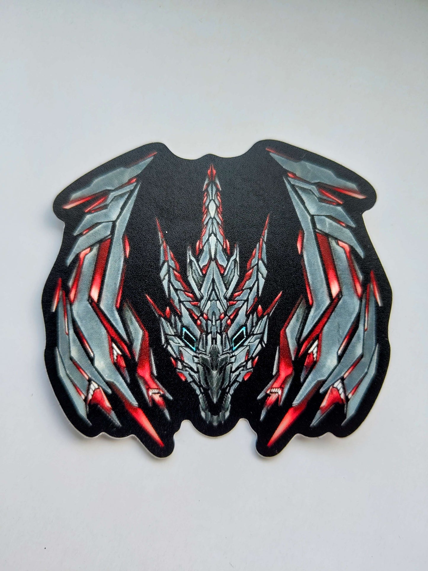A sticker with a detailed design of a stylized dragon's head and wings. The design features a dark and grey color scheme with red glowing accents. Designed by XeneDragon.