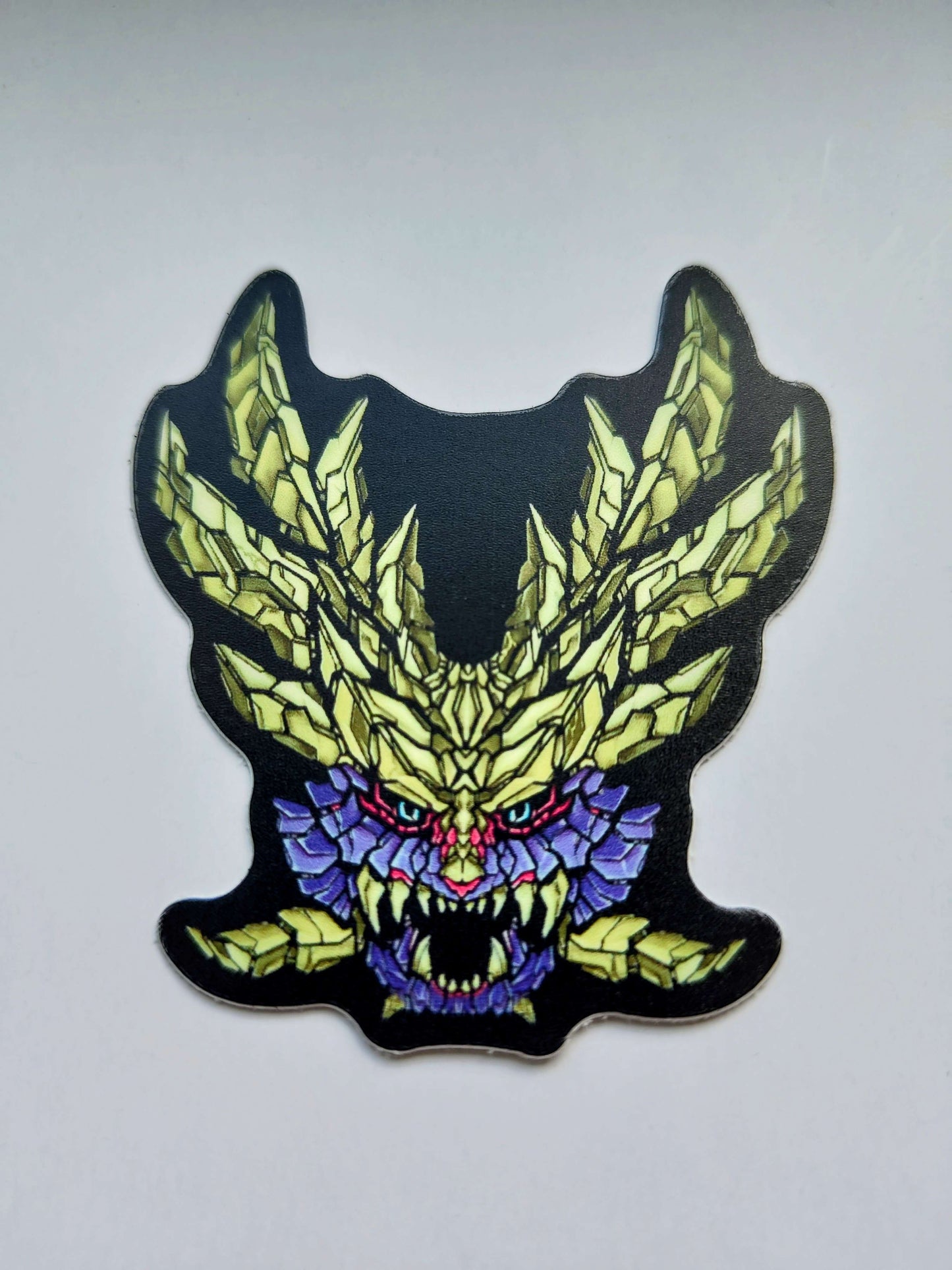 A sticker with a detailed design of a stylized monsters's head. The design features a dark purple color scheme with yellow intricate patterned horns. Designed by XeneDragon.
