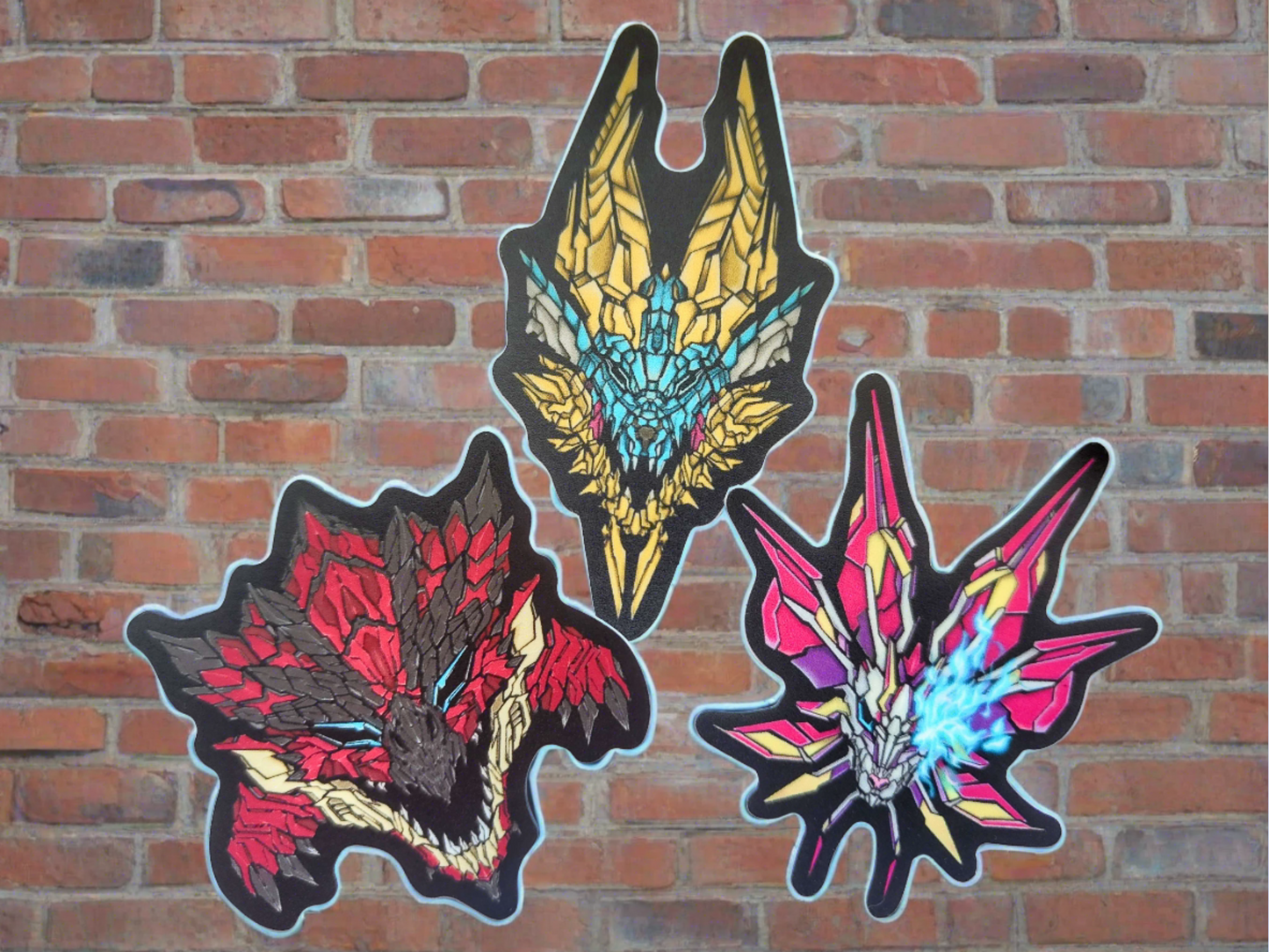 Three vibrant stickers depicting stylized monster heads are affixed to a brick wall. Each sticker showcases a unique design with distinct colors and mecha textures made by XeneDragon