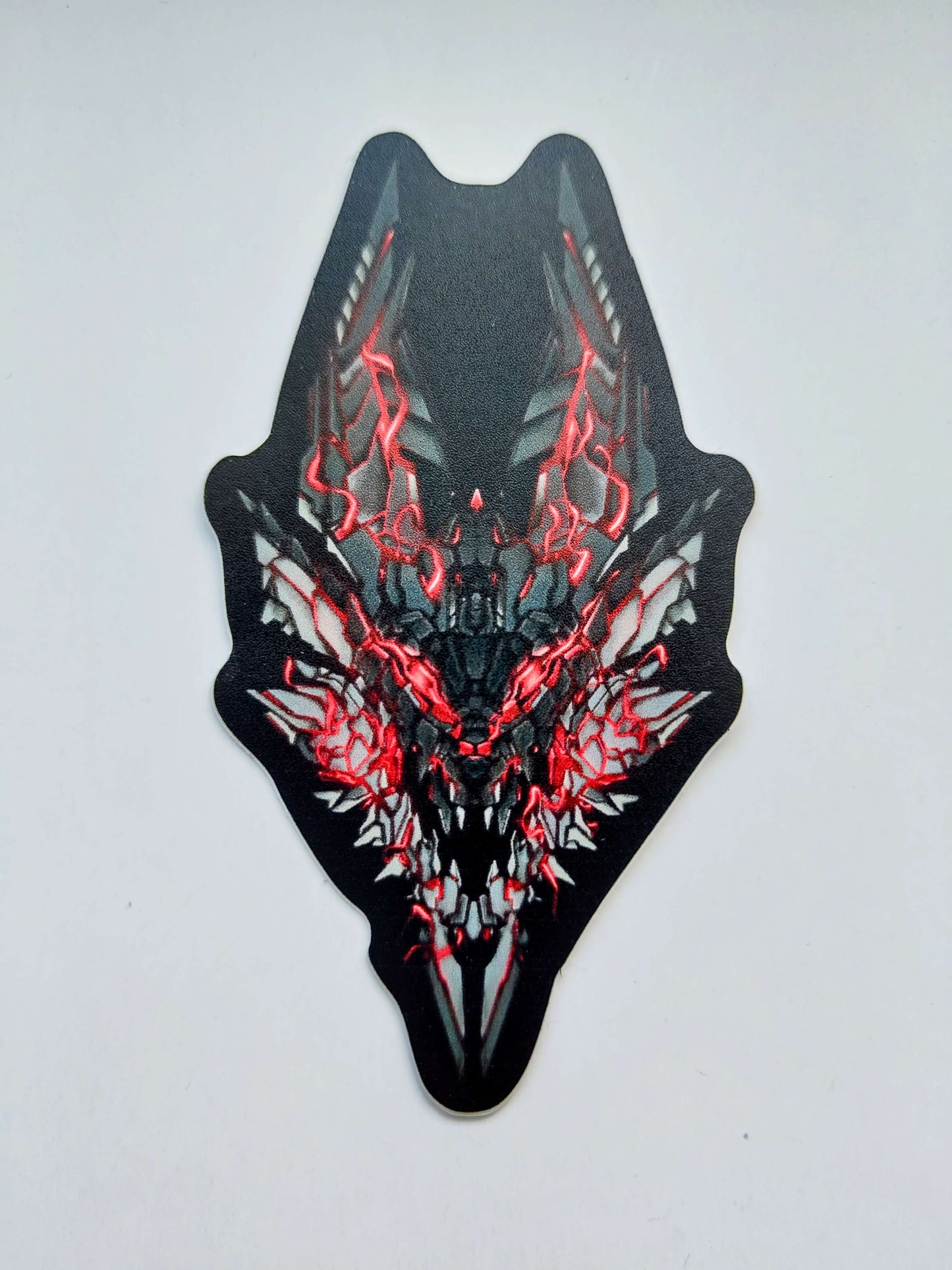 A sticker with a detailed design of a stylized monster's head. The design features a dark color scheme with red accents. Designed by XeneDragon.