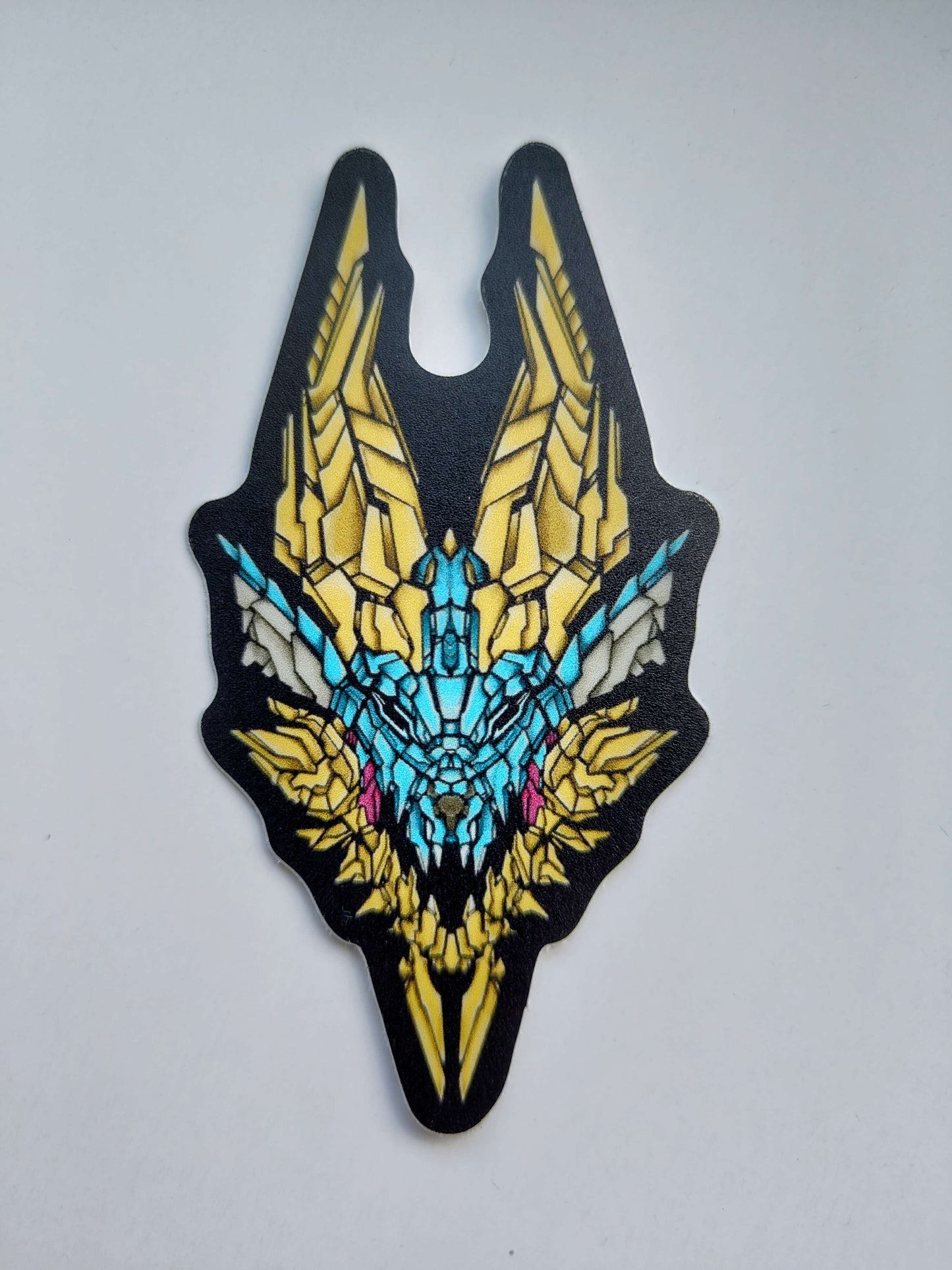 A sticker with a detailed design of a stylized monster's head. The design features vibrant colors like yellow, blue, and pink, with intricate patterns. Designed by XeneDragon