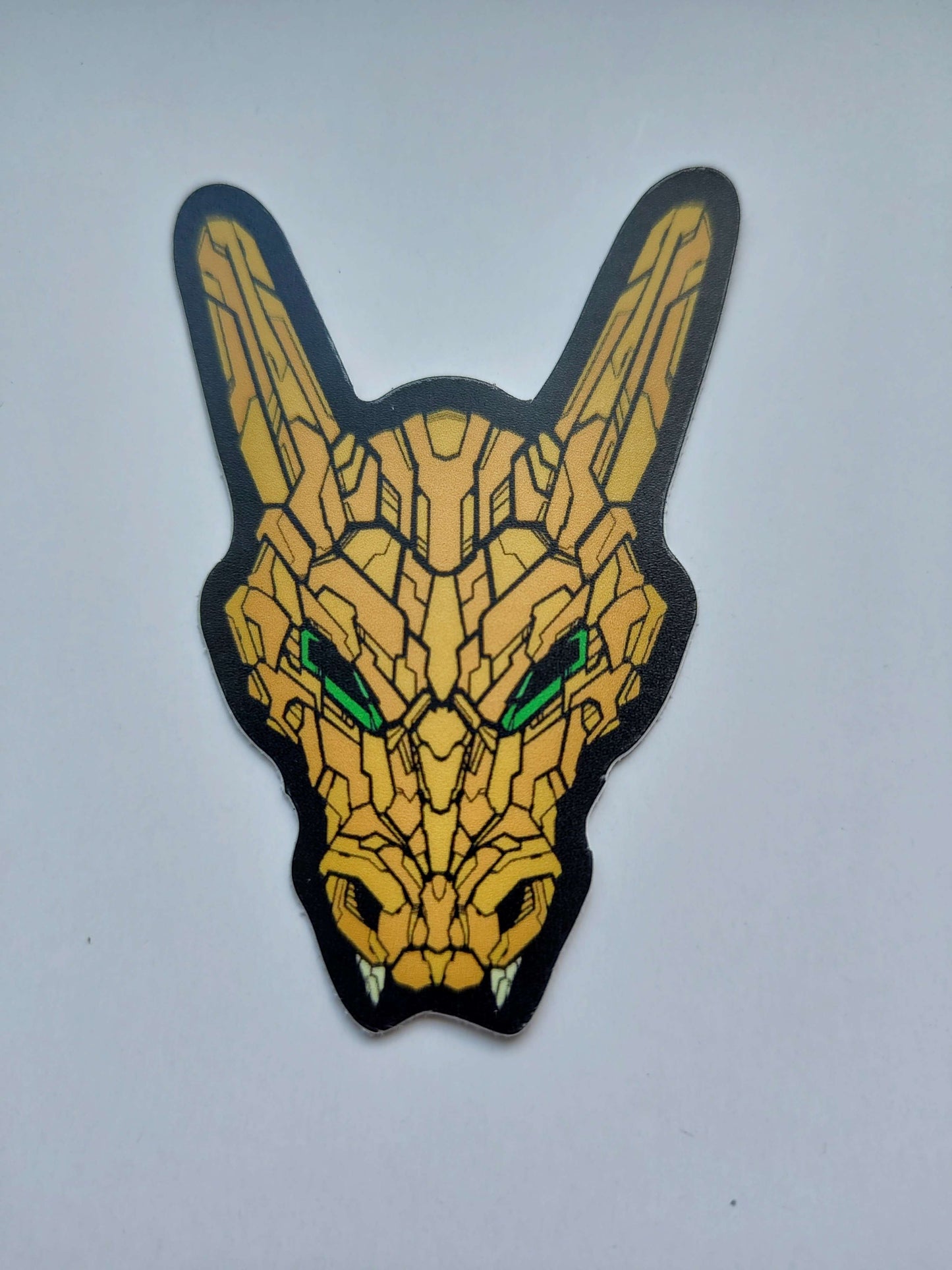 A sticker with a detailed design of a stylized dragon's head. The design features a yellow orange color scheme with green eyes. Designed by XeneDragon.
