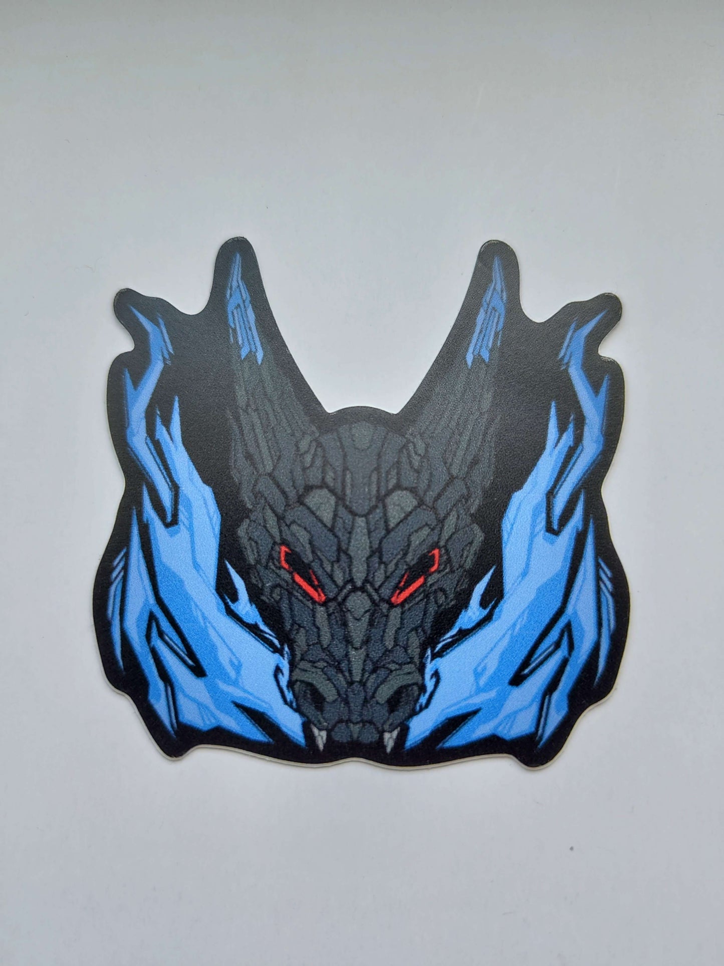 A sticker with a detailed design of a stylized dragon's head with blue flames. The design features a dark theme with greys, blue accents, and red eyes. Designed by XeneDragon.