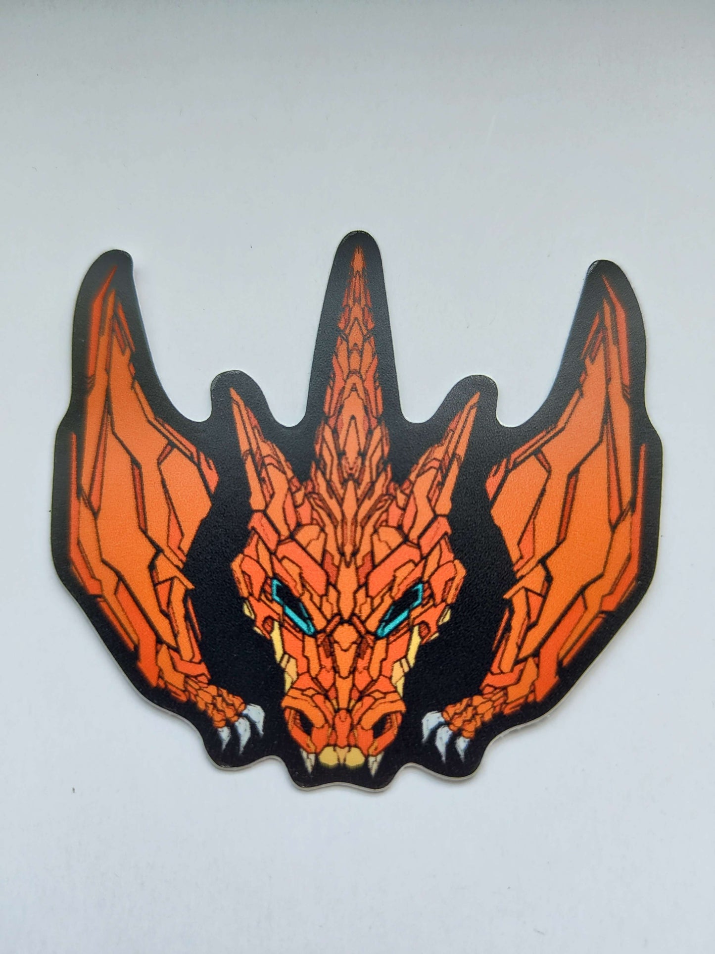 A sticker with a detailed design of a stylized dragon's head with wings. The design features a vibrant orange color scheme with blue eyes. Designed by XeneDragon.