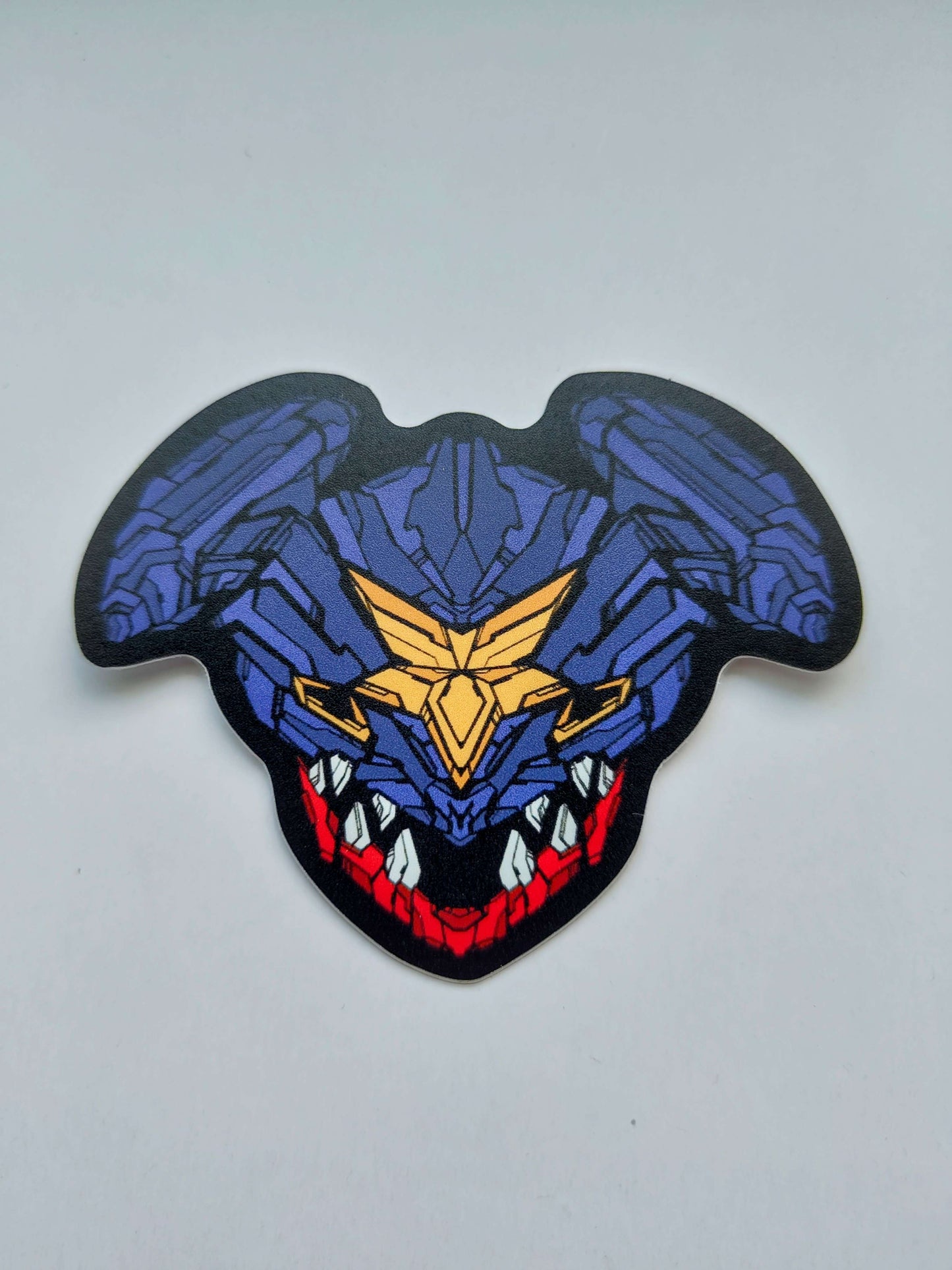 A sticker with a detailed design of a stylized creature's head. The design features a dark color scheme with purple, yellow, and red accents. Designed by XeneDragon
