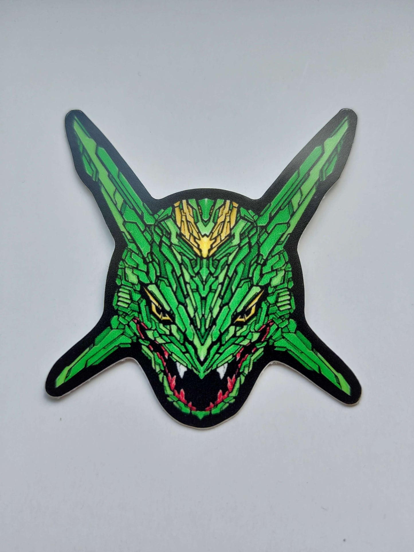 A sticker with a detailed design of a stylized dragon's head. The design features a vibrant green color scheme with yellow and red accents. Designed by XeneDragon.