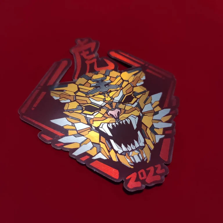 A special metallic effect sticker with a vibrant geometric design celebrating the Year of the Tiger. The sticker features a stylized image of a tiger's head in gold, with the Chinese character for "tiger" and the year "2022" printed below in red. Designed by XeneDragon