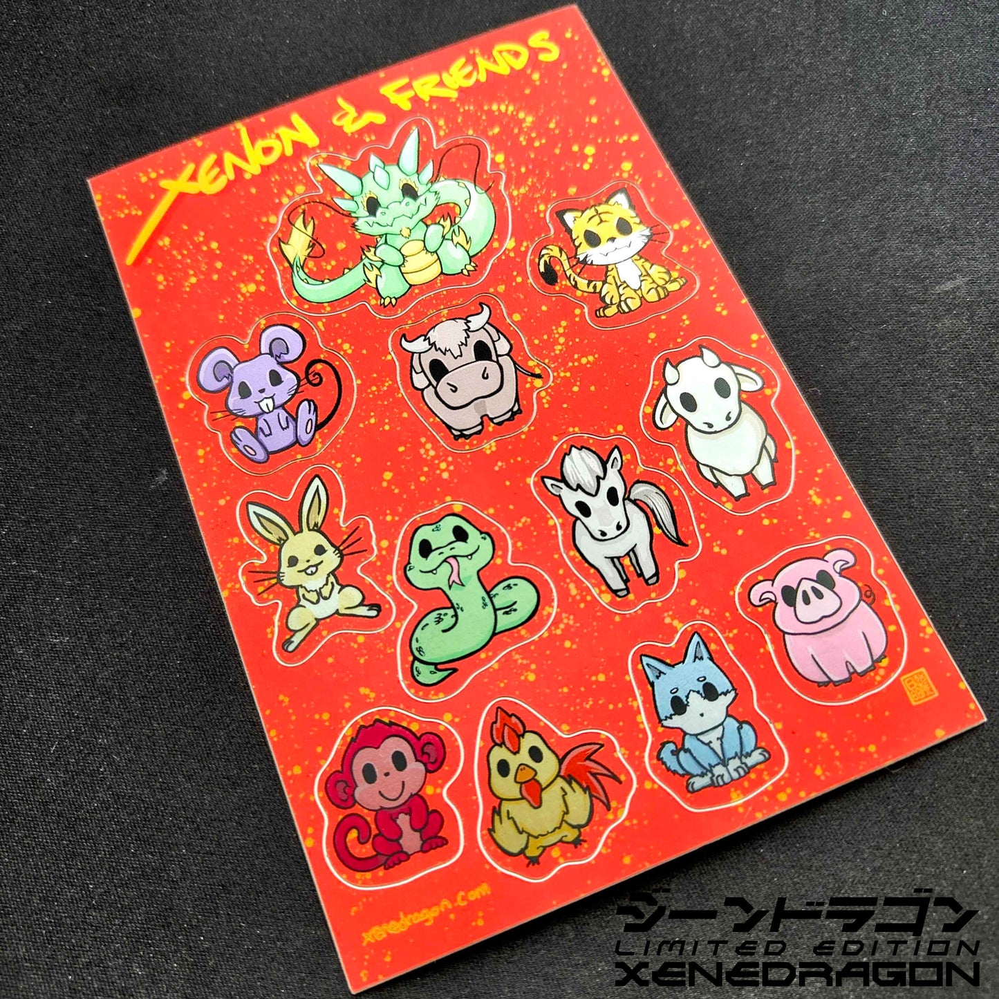 A sticker sheet containing the 12 animals of the lunar zodiac: Dragon, Mouse, Ox, Tiger, Hare, Snake, Horse, Ram, Monkey, Chicken, Dog, and Boar. The design has a bright red background with golden dots. Made by XeneDragon.