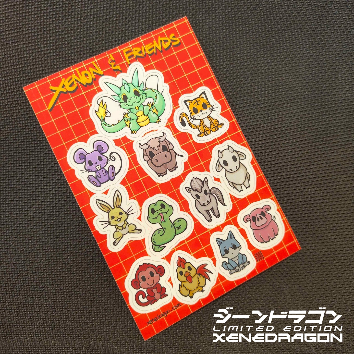 A sticker sheet containing the 12 animals of the lunar zodiac: Dragon, Mouse, Ox, Tiger, Hare, Snake, Horse, Ram, Monkey, Chicken, Dog, and Boar. The design has a bright red background with golden dots. Made by XeneDragon. This picture shows the actual misprint version product.