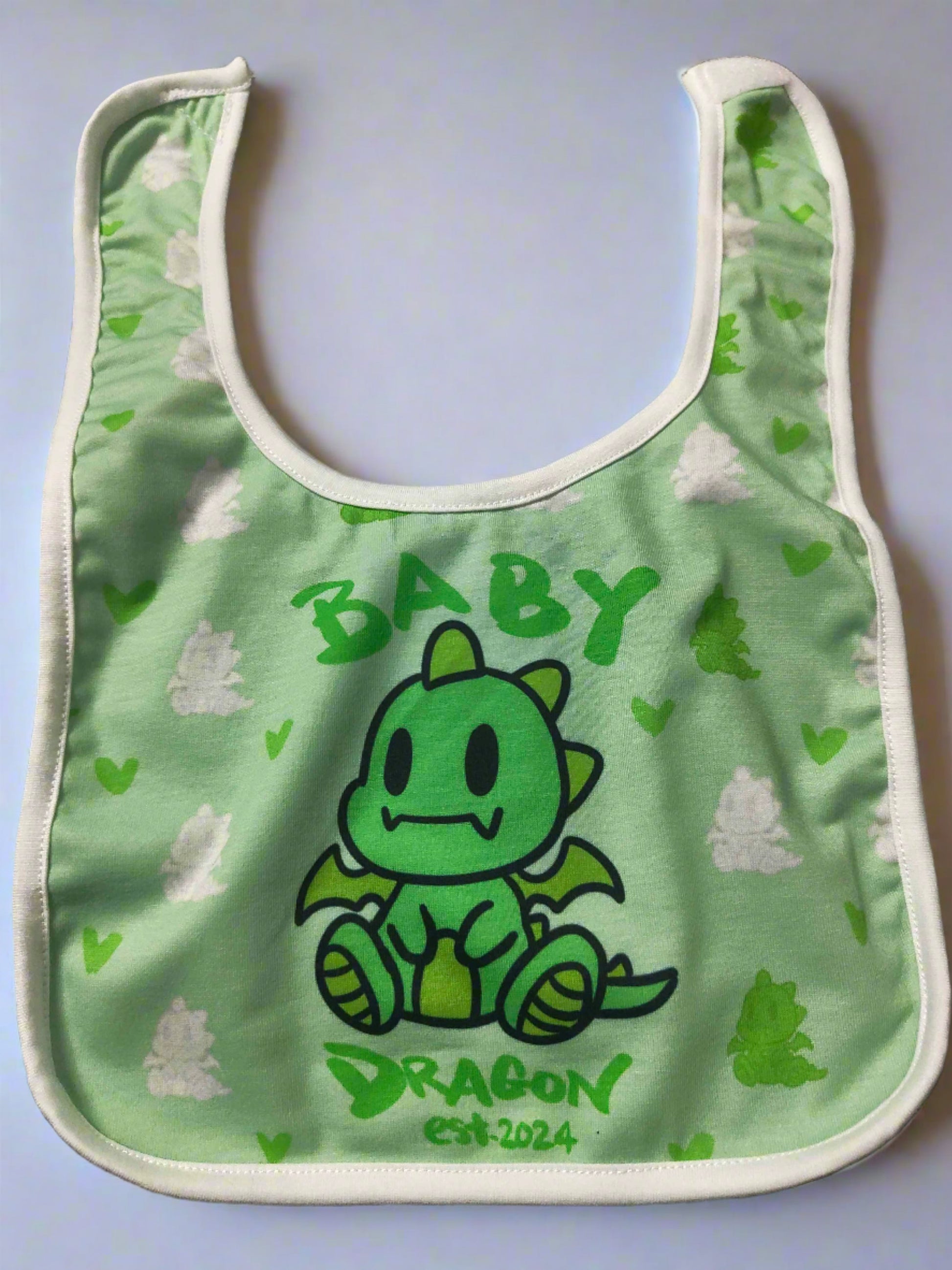 A green baby bib with a white border. It features a cartoon green dragon in the center with the word "BABY" written above it and "DRAGON est. 2024" written below it.