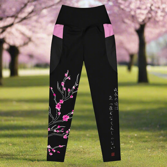 A pair of black leggings with cherry blossom branch on the left leg and Japanese text that translates to "Growth is non-linear"