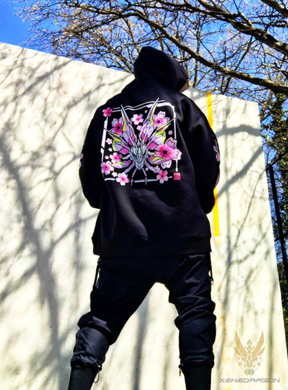 A picture of a model wearing a hoodie in the park with blue sky and trees in the background. The model is facing away to showcase the back of the design