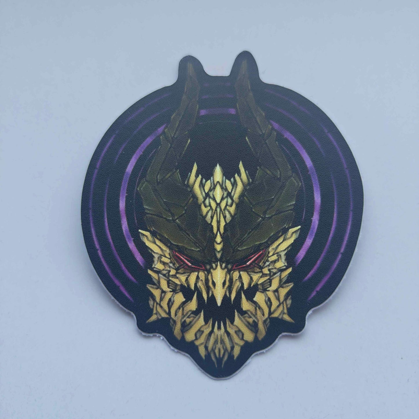 A special iridescent effect sticker with a detailed design of a stylized creature's head. The design features a dark background with a golden dragon head with a purple circular designs behind the dragon's head. Designed by XeneDragon.