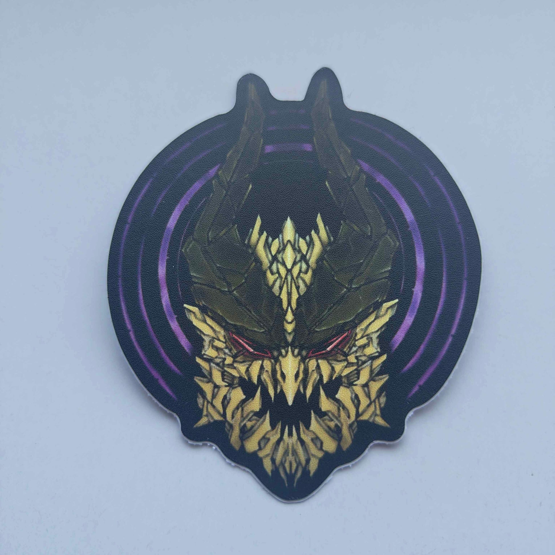 A special iridescent effect sticker with a detailed design of a stylized creature's head. The design features a dark background with a golden dragon head with a purple circular designs behind the dragon's head. Designed by XeneDragon.