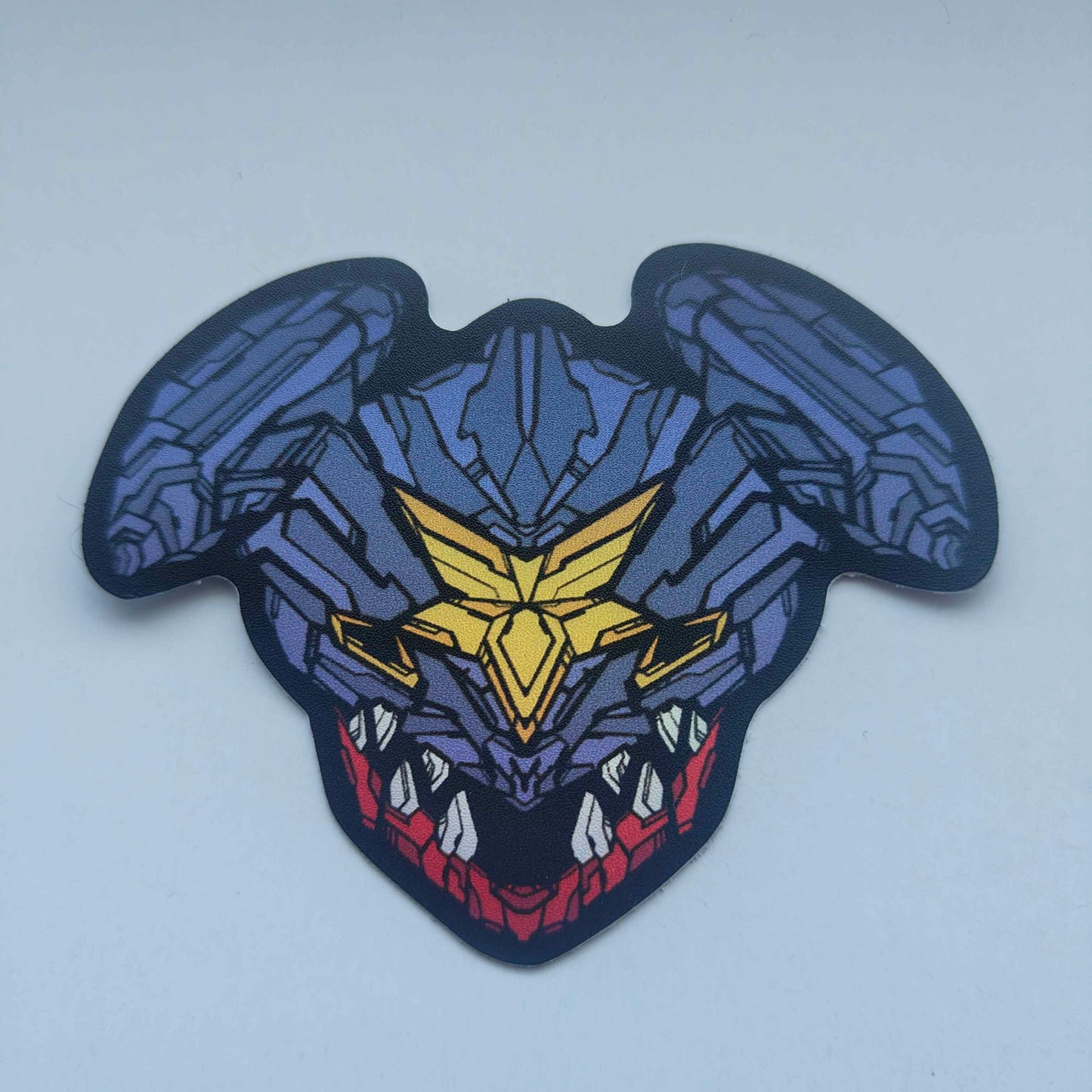 A special iridescent effect sticker with a detailed design of a stylized creature's head. The design features a dark color scheme with purple, yellow, and red accents. Designed by XeneDragon.
