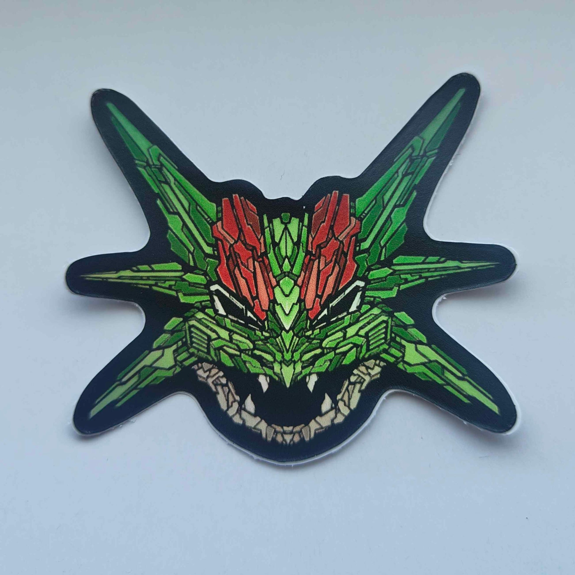 A special iridescent effect sticker with a detailed design of a stylized dragon's head. The design features a vibrant green and red color scheme. Designed by XeneDragon.